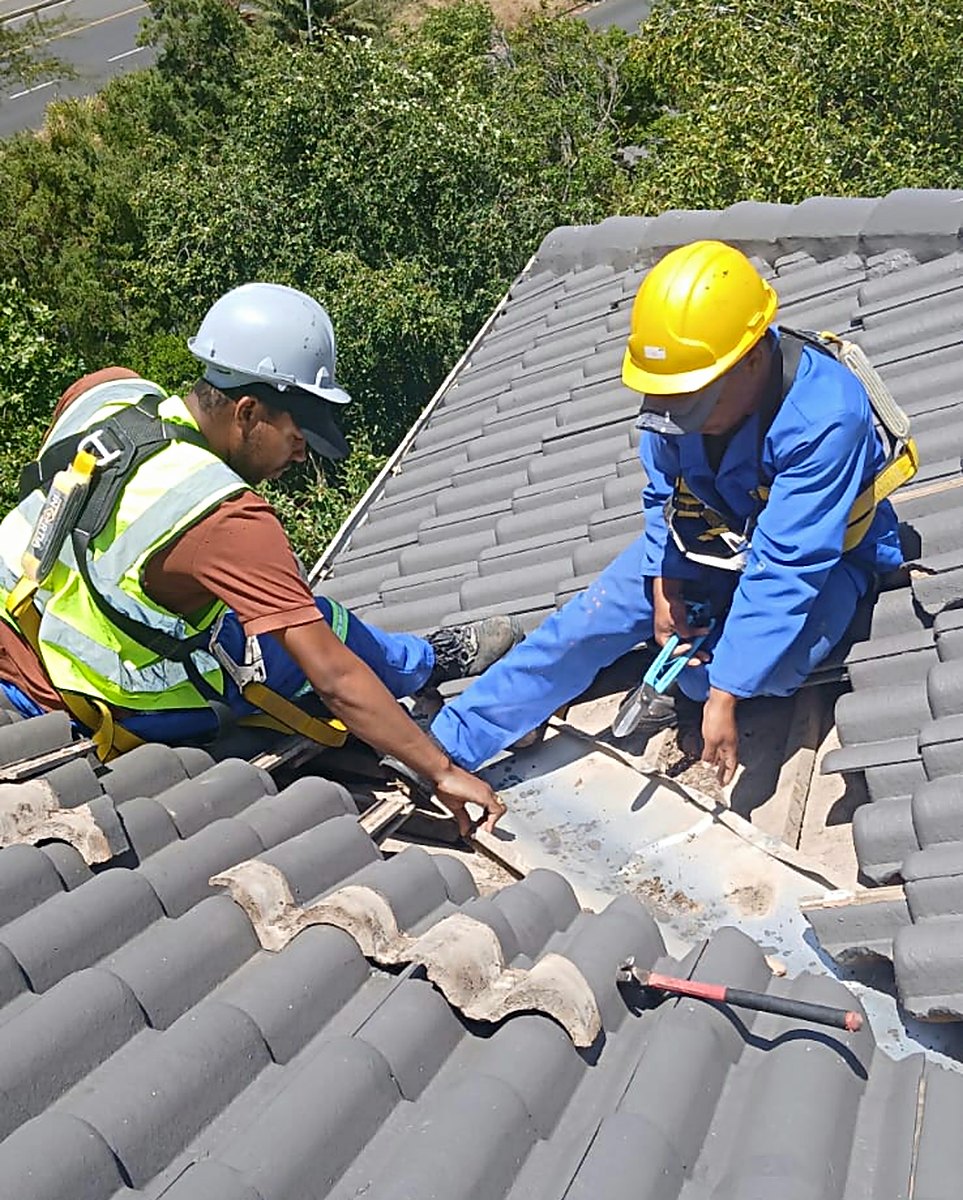 Two roofers in hard hats and harnesses repairing a valley on a concrete tile roof