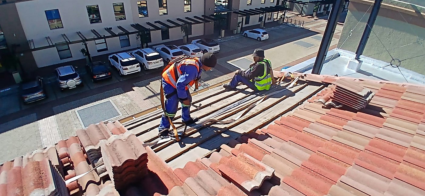 Roofers replacing concrete roof tiles above a parking area