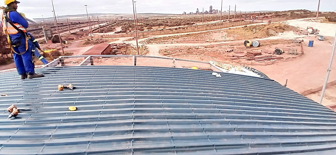 Roofer in a safety harness on a curved industrial sheeted roof