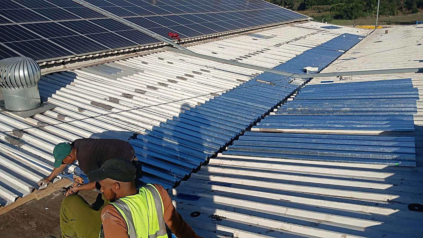 New roof sheets being fitted next to a solar panel array